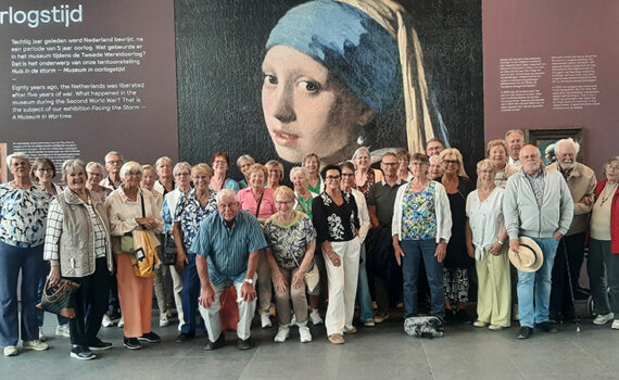 Groepsfoto van leden van VVS Hillegom bij een grote afbeelding van Het Meisje met de Parel van Johannes Vermeer.