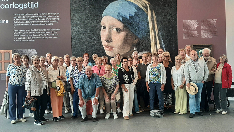 Groepsfoto van leden van VVS Hillegom bij een grote afbeelding van Het Meisje met de Parel van Johannes Vermeer.