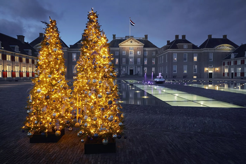 Paleis Het Loo in de schemering met op de voorgrond twee verlichte kerstbomen.