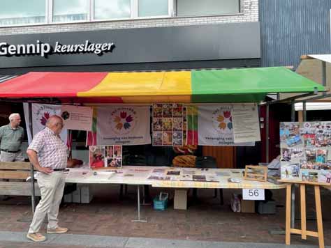 Kraam van VVS Hillegom tijdens de jaarmarkt in Hillegom. Er liggen tal van folders, een grote collage met foto's van de activiteiten. Johan de Groot staat links naast de kraam en ervoor voorzitter Frans van Lierop. De luifel is rood, geel, groen gestreept.