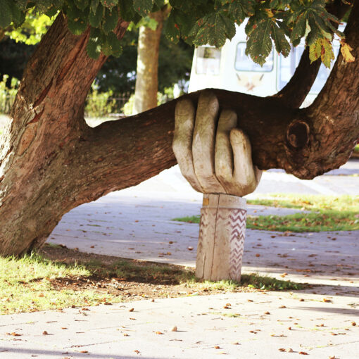 Beeld van overhangende boom waarbij de onderste tak wordt ondersteund door een grote uit hout gesneden hand.