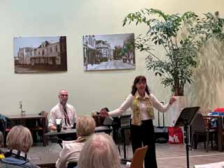 Koorleidster met daarachter pianist voor een groep bejaarden.