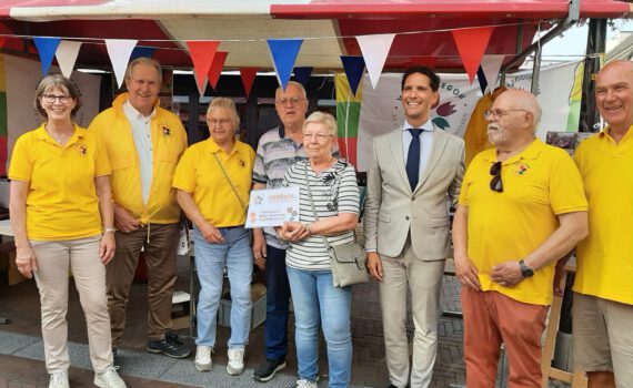 Bestuur van VVS Hillegom in hun felgele t-shirts met in het midden een senior echtpaar en de burgemeester in een cremekleurig pak.